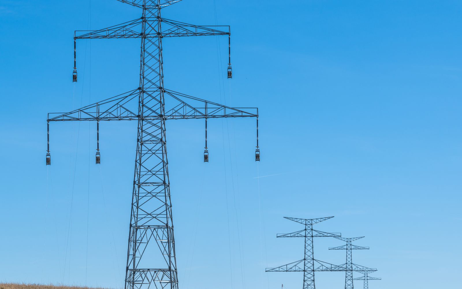 High-voltage lattice transmission towers crossing dry Texas rangeland under a clear sky