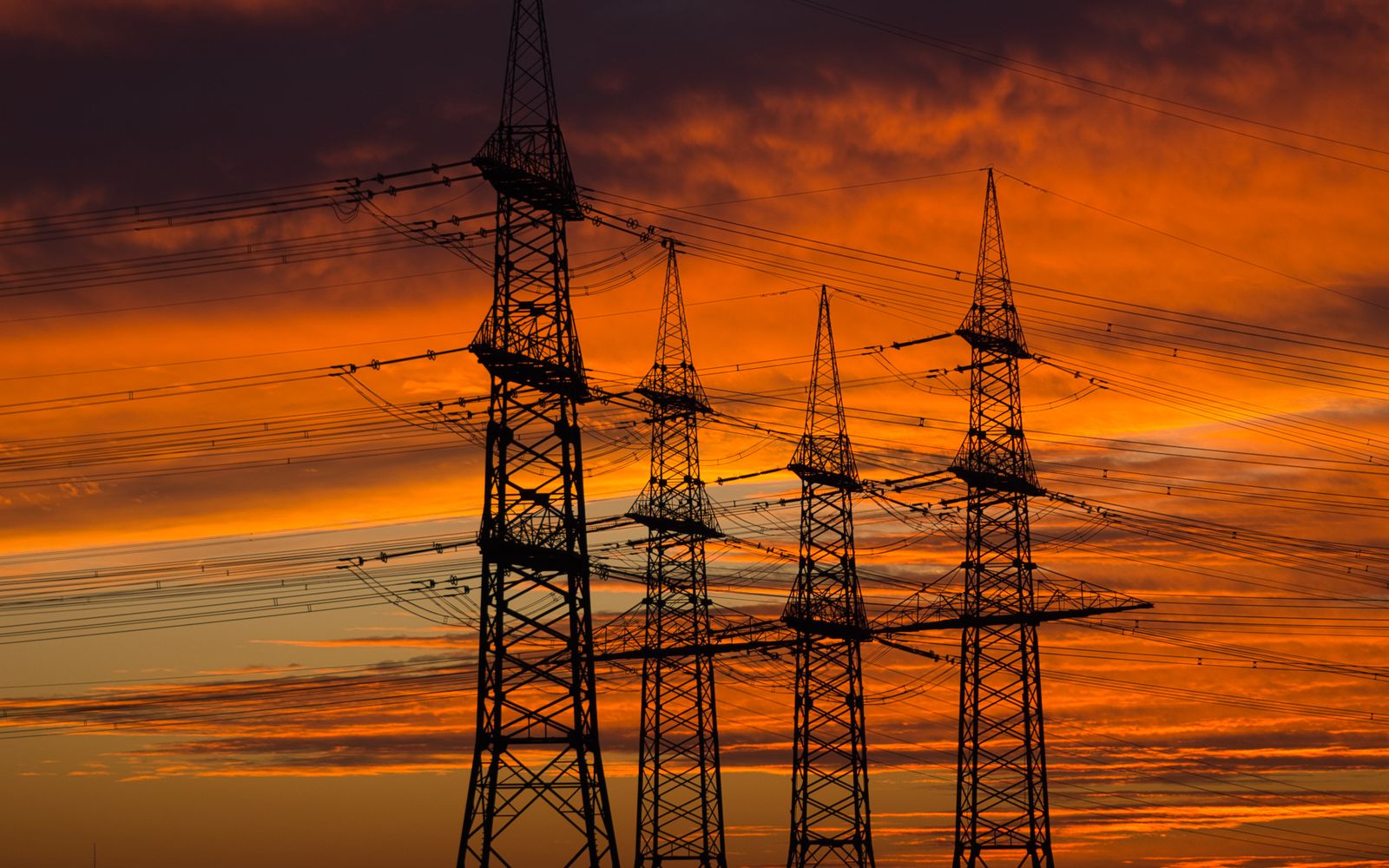 Silhouetted high-voltage transmission towers against an orange Texas sunset